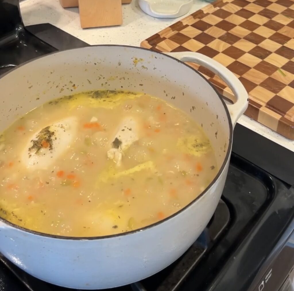 Chicken breasts simmering in broth with vegetables and Italian seasoning.