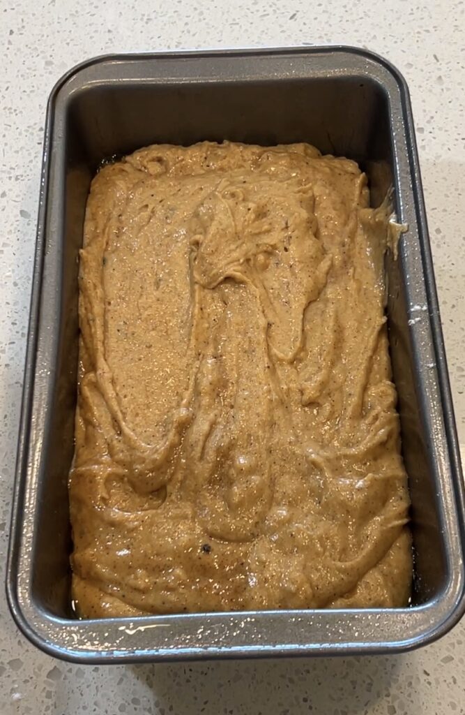 Pumpkin bread batter spread evenly into a parchment-lined loaf pan before baking.