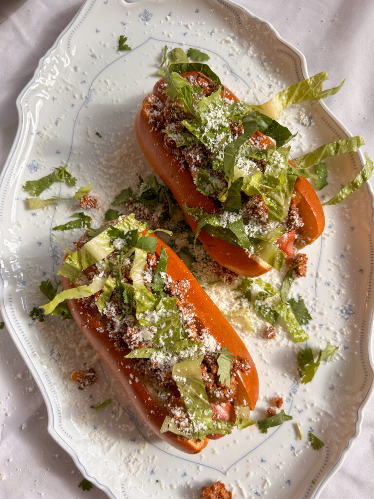 Taco dogs loaded with seasoned ground beef, shredded cheese, salsa verde, lettuce, and crunchy tortilla chips in toasted buns.
