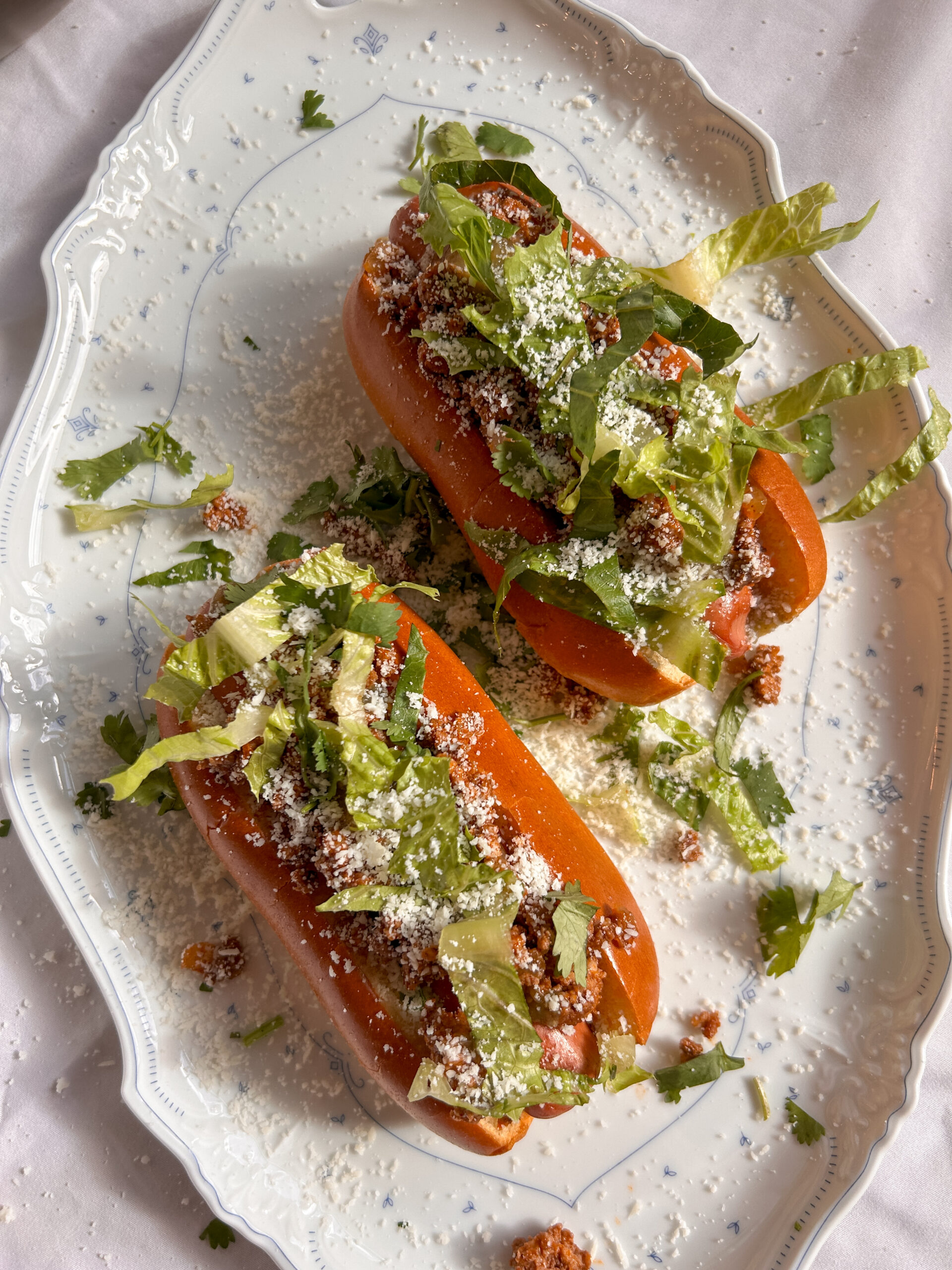 Taco dogs loaded with seasoned ground beef, shredded cheese, salsa verde, lettuce, and crunchy tortilla chips in toasted buns.